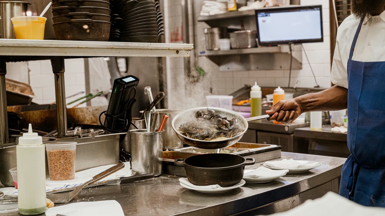 A cook working the pass, a pan going out under the ticket screen